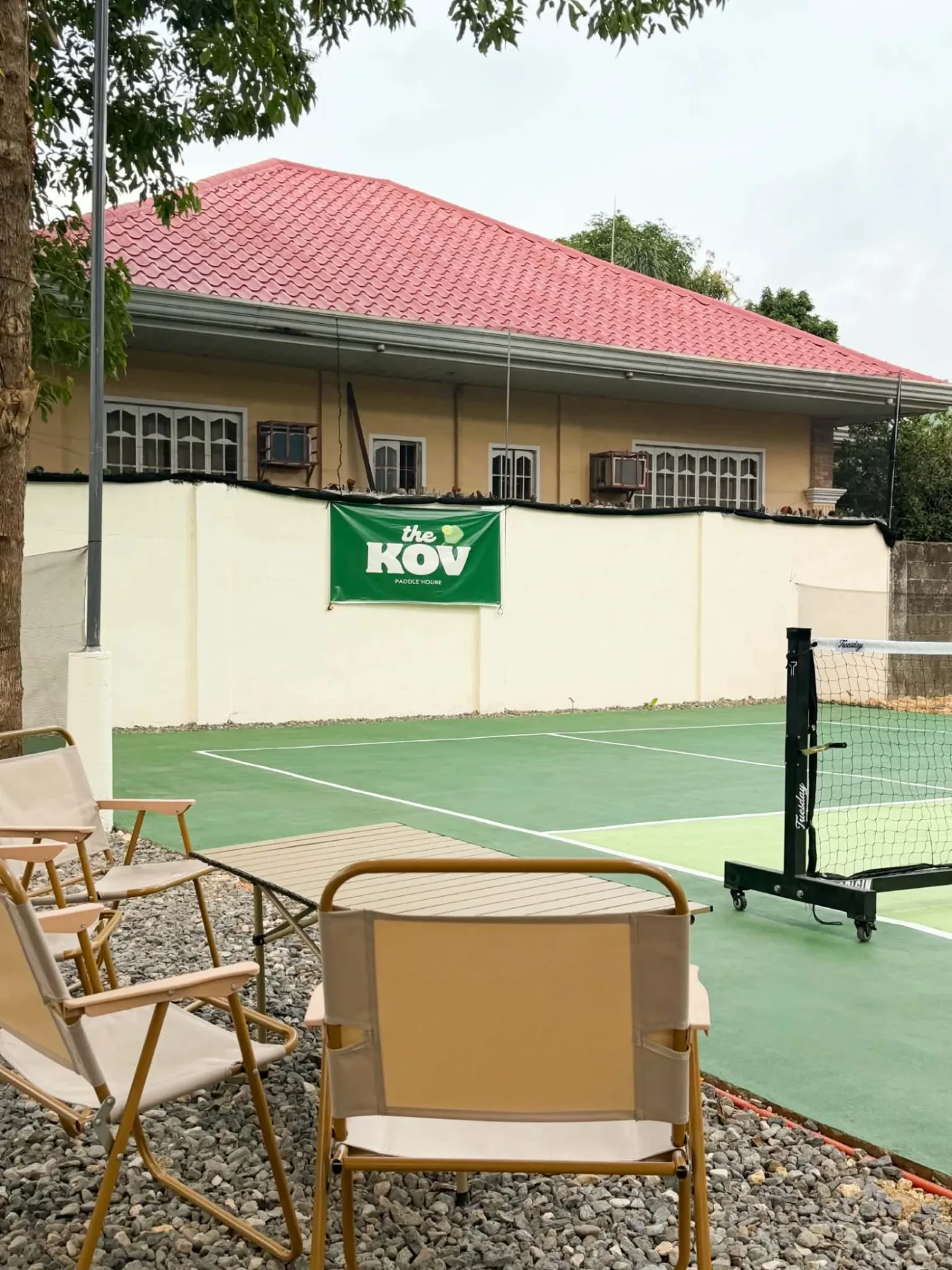The Kov's outdoor court with the club banner on the wall and camp chairs courtside